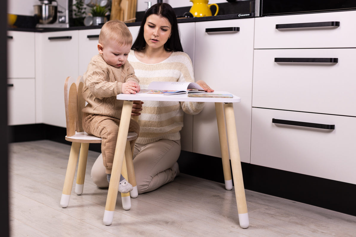 Een kind tekent aan de witte Bunny tafel op één stoel met konijnenoren, met een volwassene ernaast.