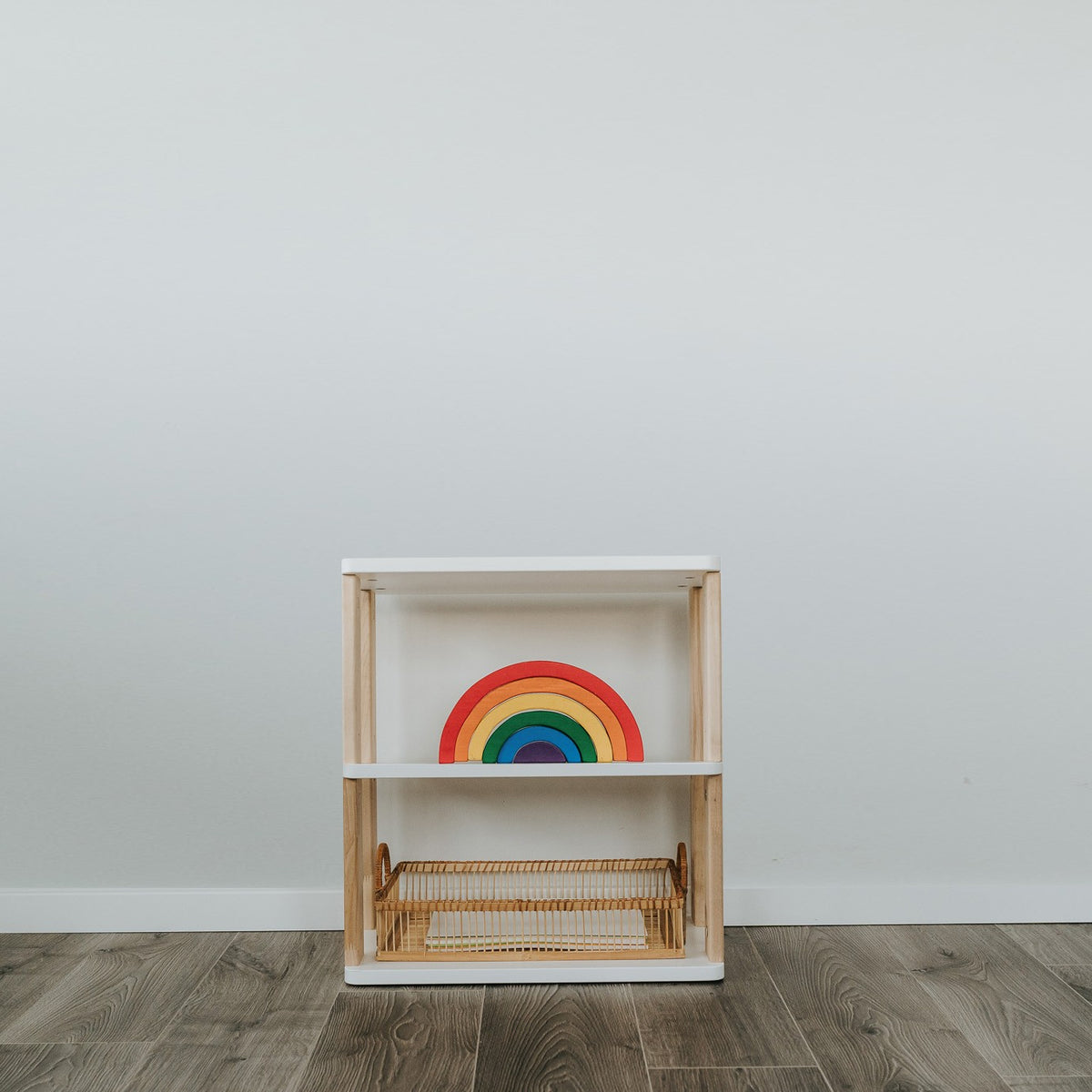 Straight Mini kast met drie witte planken en houten zijkanten, met een speelgoedregenboog en een rieten mand.