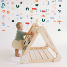 Child playing with a wooden climbing toy against a colorful alphabet wall.