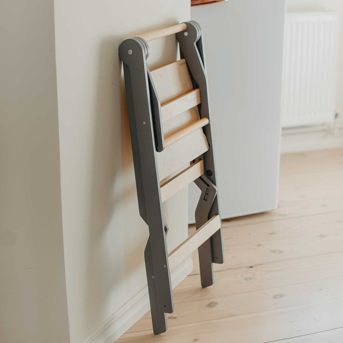Gray ZigZag foldable learning tower stored folded flat against a wall